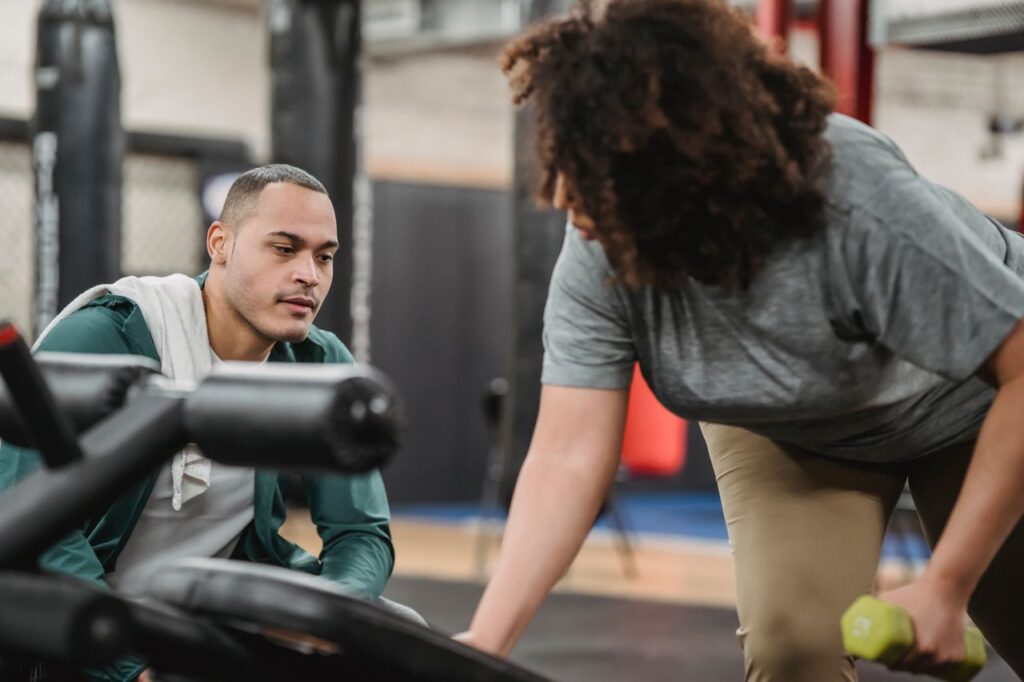 Coach closely guiding a woman through a dumbbell exercise at the gym